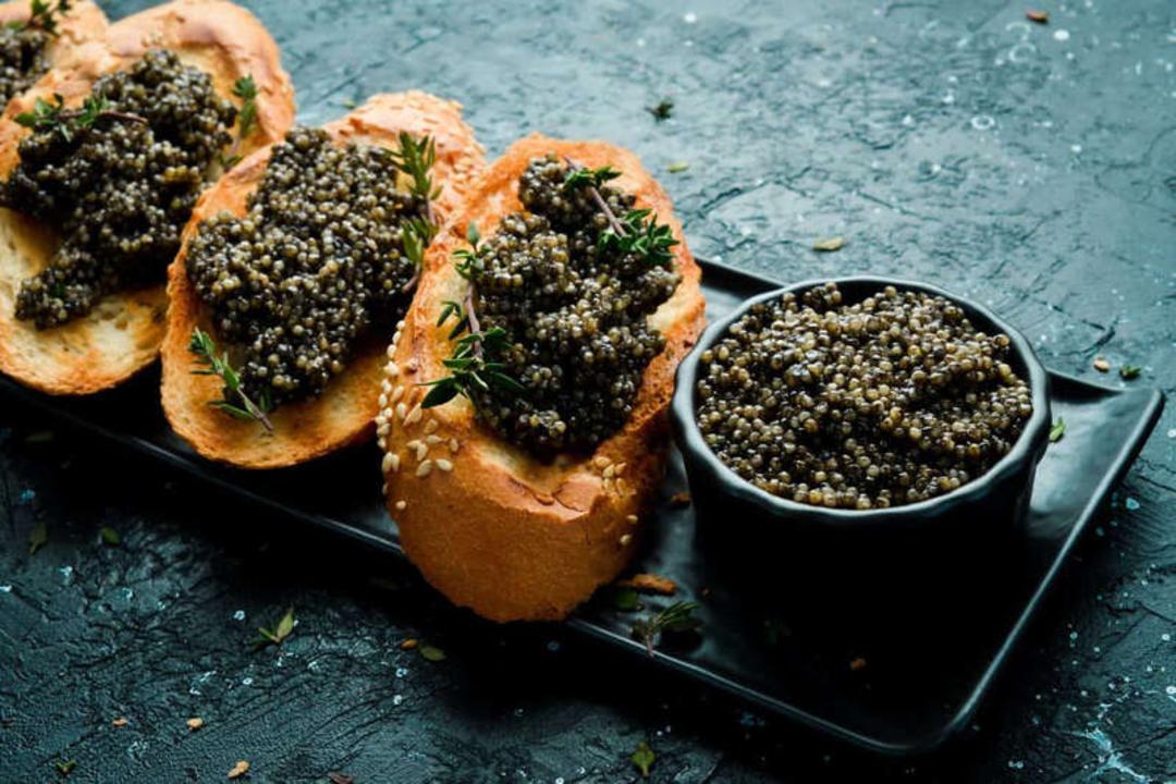 خاویار (Caviar) سیاه روی تکه‌های نان تست و در یک ظرف کوچک