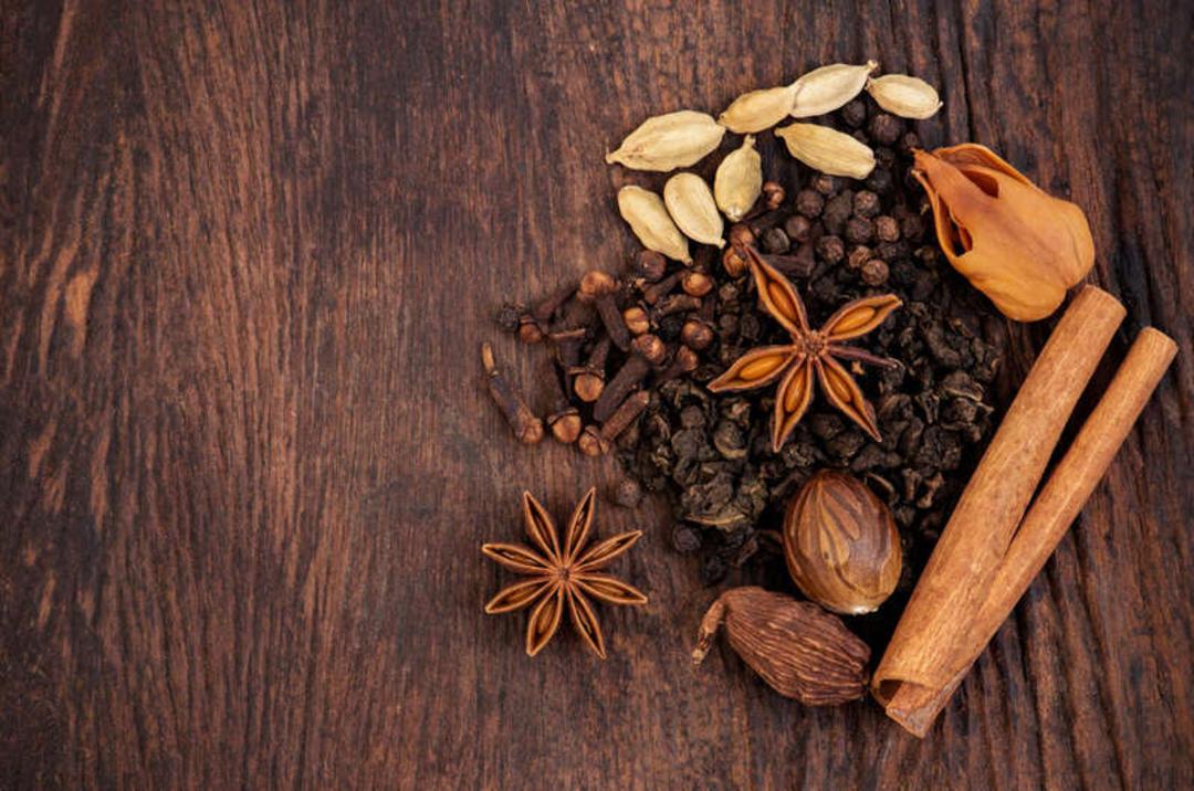 ادویه‌های مختلف چای ماسالا شامل دارچین، انیسون ستاره‌ای و هل روی سطح چوبی
