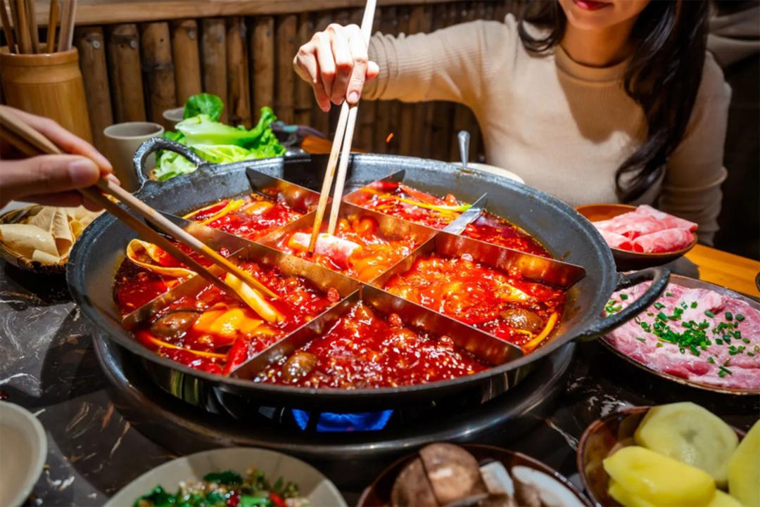 دیگ هات‌پات (Hotpot) پر از سوپ تند و مواد غذایی متنوع