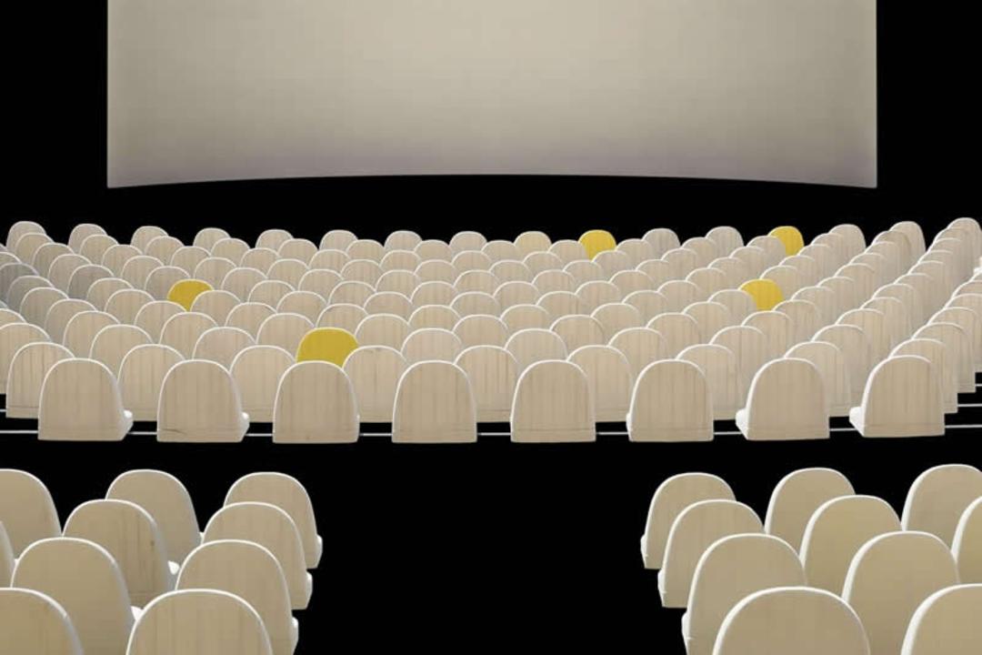 صندلی‌های سفید سالن سینما در مقابل پرده نمایش بزرگ
