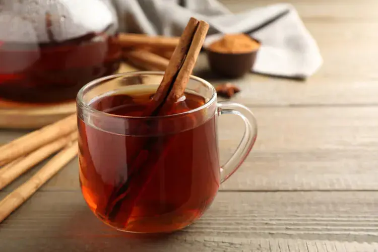 نوشیدنی گرم دارچین در لیوان شیشه‌ای روی میز چوبی