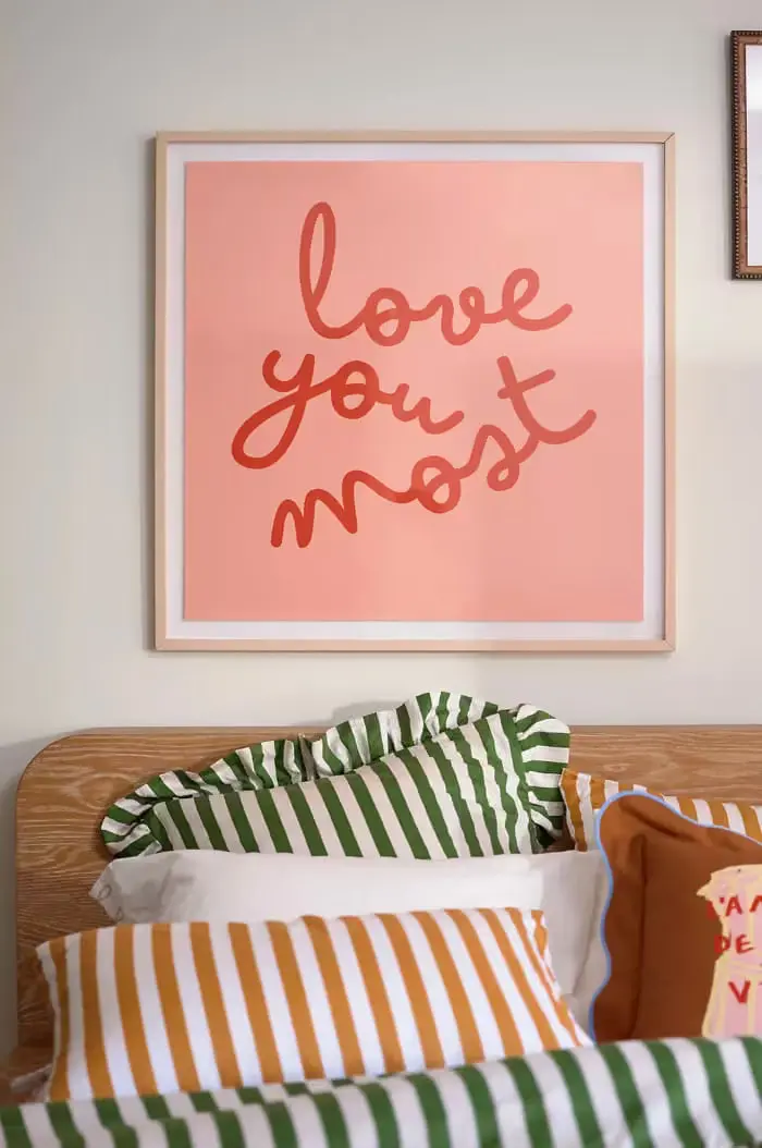 تابلو دیوار با متن love you most بالای تخت خواب با ملحفه‌های راه راه