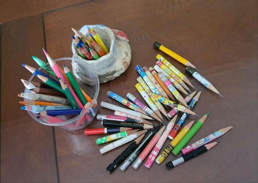 مداد رنگی‌های متنوع در ظرف پلاستیکی و روی میز چوبی