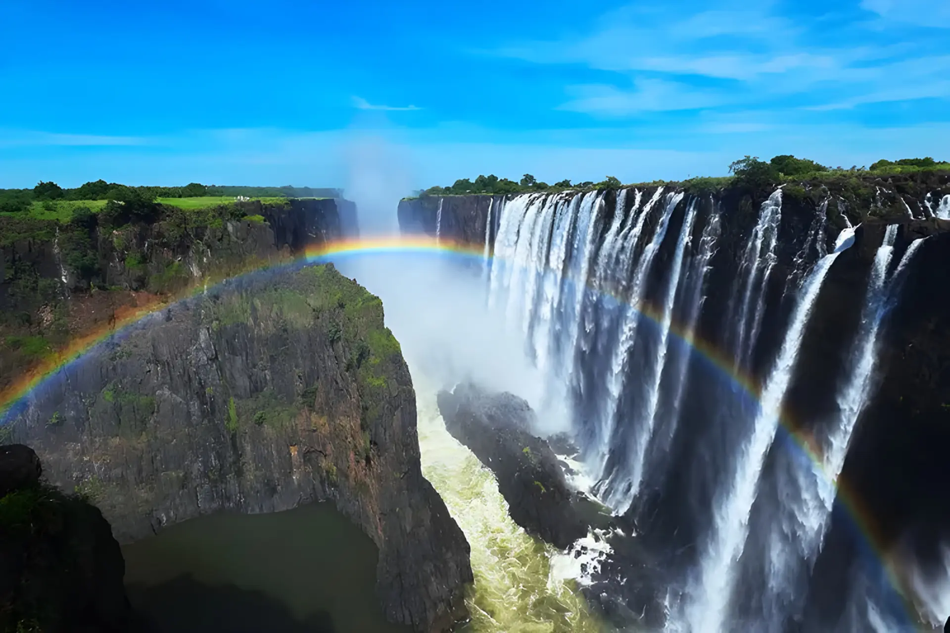 آبشار ویکتوریا (Victoria Falls) با قوس رنگین‌کمان در میان مه و صخره‌ها