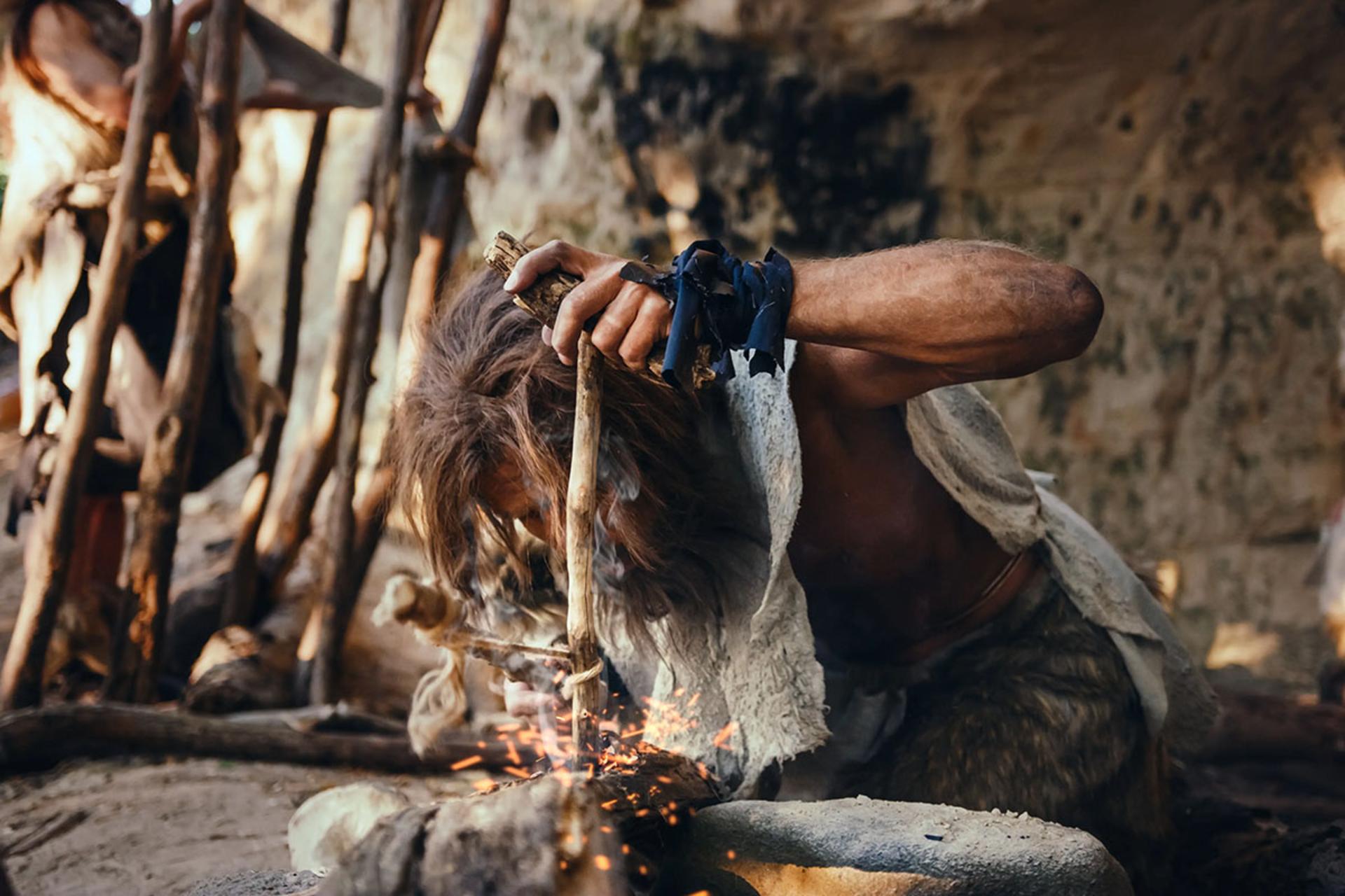 نمای نزدیک از یک انسان اولیه در حال تلاش برای روشن کردن آتش با ابزار بدوی