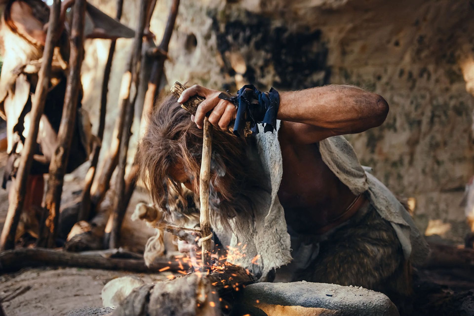 نمای نزدیک از یک انسان اولیه در حال تلاش برای روشن کردن آتش با ابزار بدوی