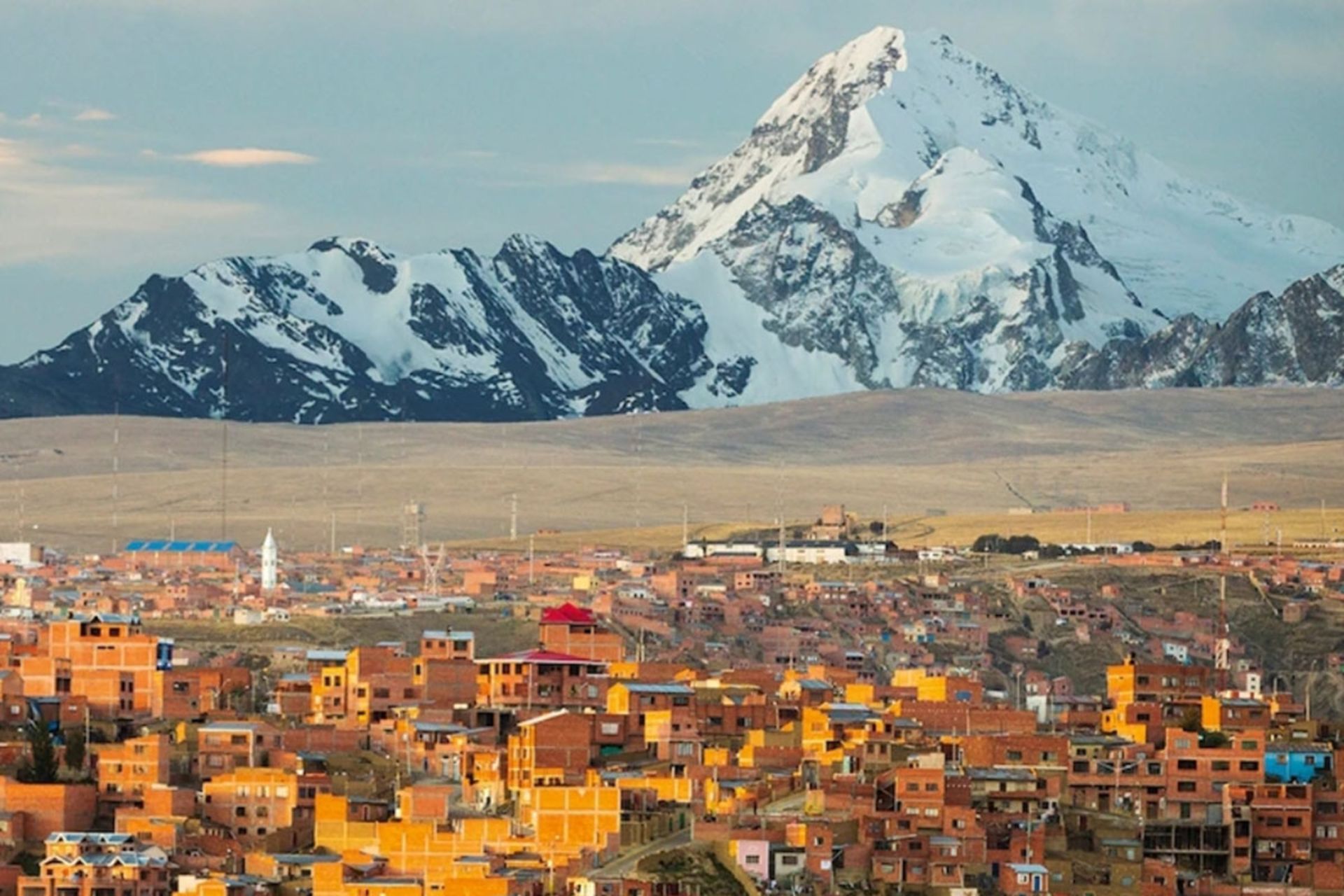 خانه‌های آجری فشرده در پیش‌زمینه و قله برفی و باشکوه ایلیمانی بولیوی در پس‌زمینه