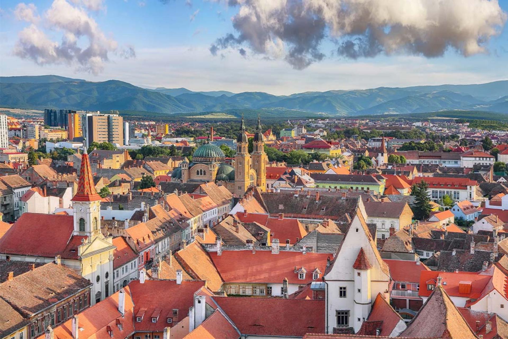 نمای پانوراما از سقف‌های قرمز شهر قدیمی سیبیو (رومانی) با کوه‌های پس‌زمینه