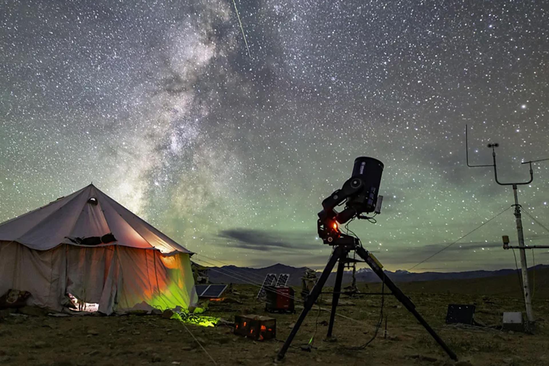 چادری روشن از داخل و یک تلسکوپ در فضای باز زیر آسمان پرستاره هانله