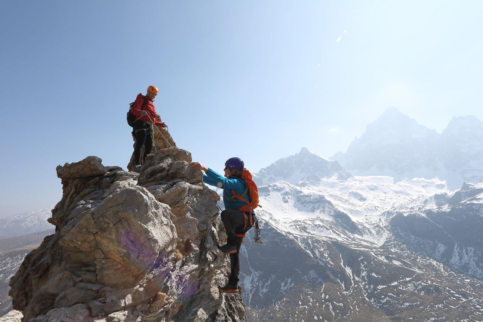 دو کوهنورد با تجهیزات کامل در حال صعود از صخره‌های مرتفع یک قله کوهستانی برفی