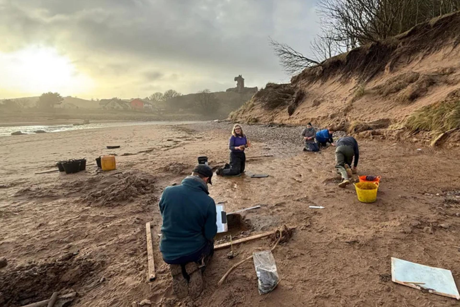 گروهی از باستان‌شناسان در یک روز ابری و مه‌آلود، روی زمین گلی و مرطوب ساحل لونان