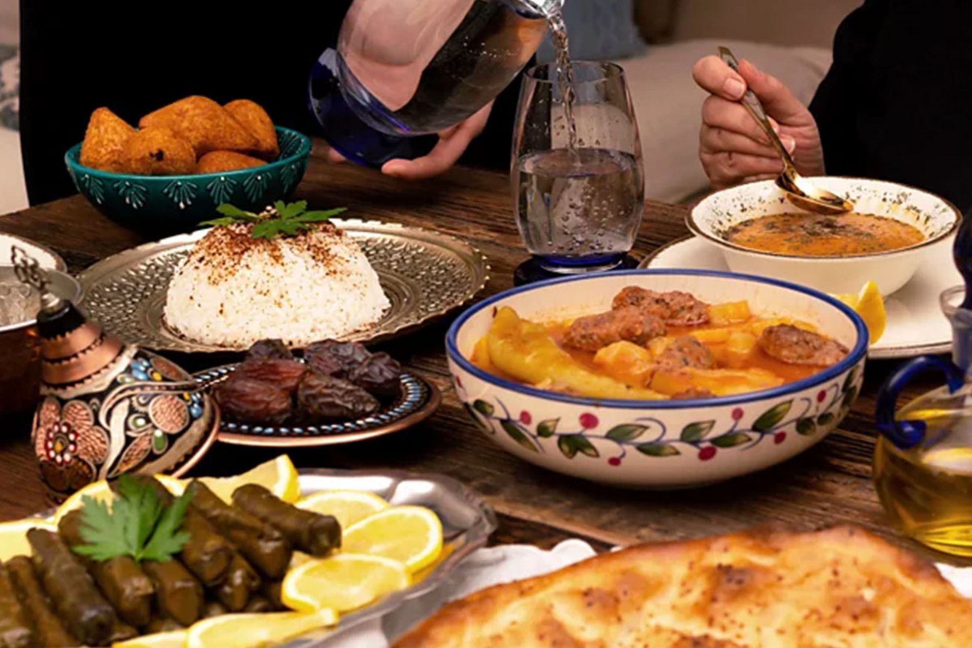 سفره‌ای رنگین از غذاهای خاورمیانه‌ای شامل دیس دلمه برگ مو، برنج تزیین شده، سوپ و خرما