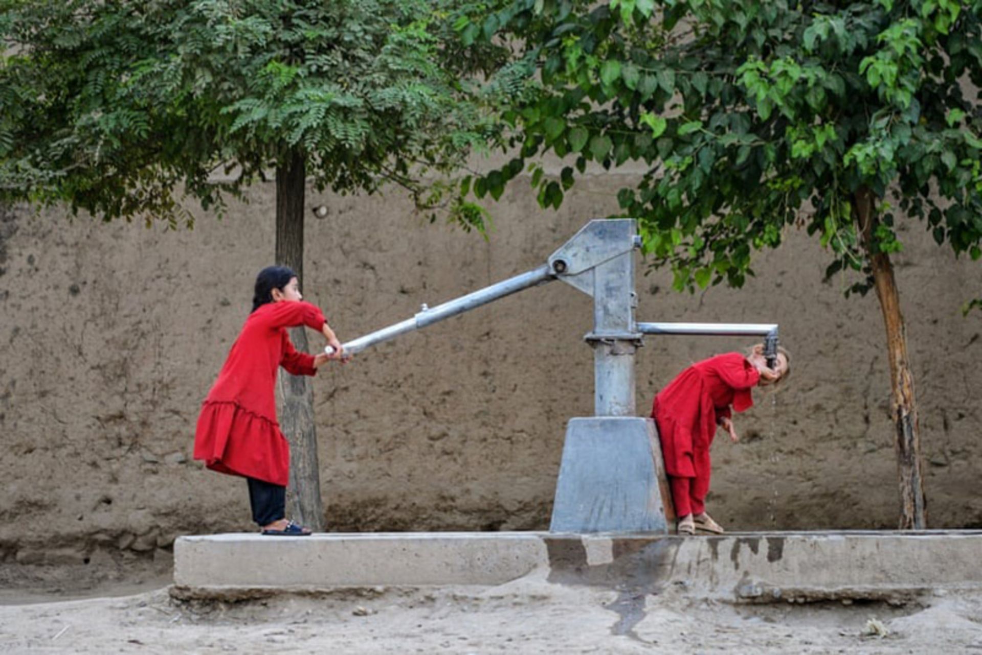 دختری در فیض‌آباد افغانستان، در میان خشکسالی در حال نوشیدن آب از یک پمپ دستی