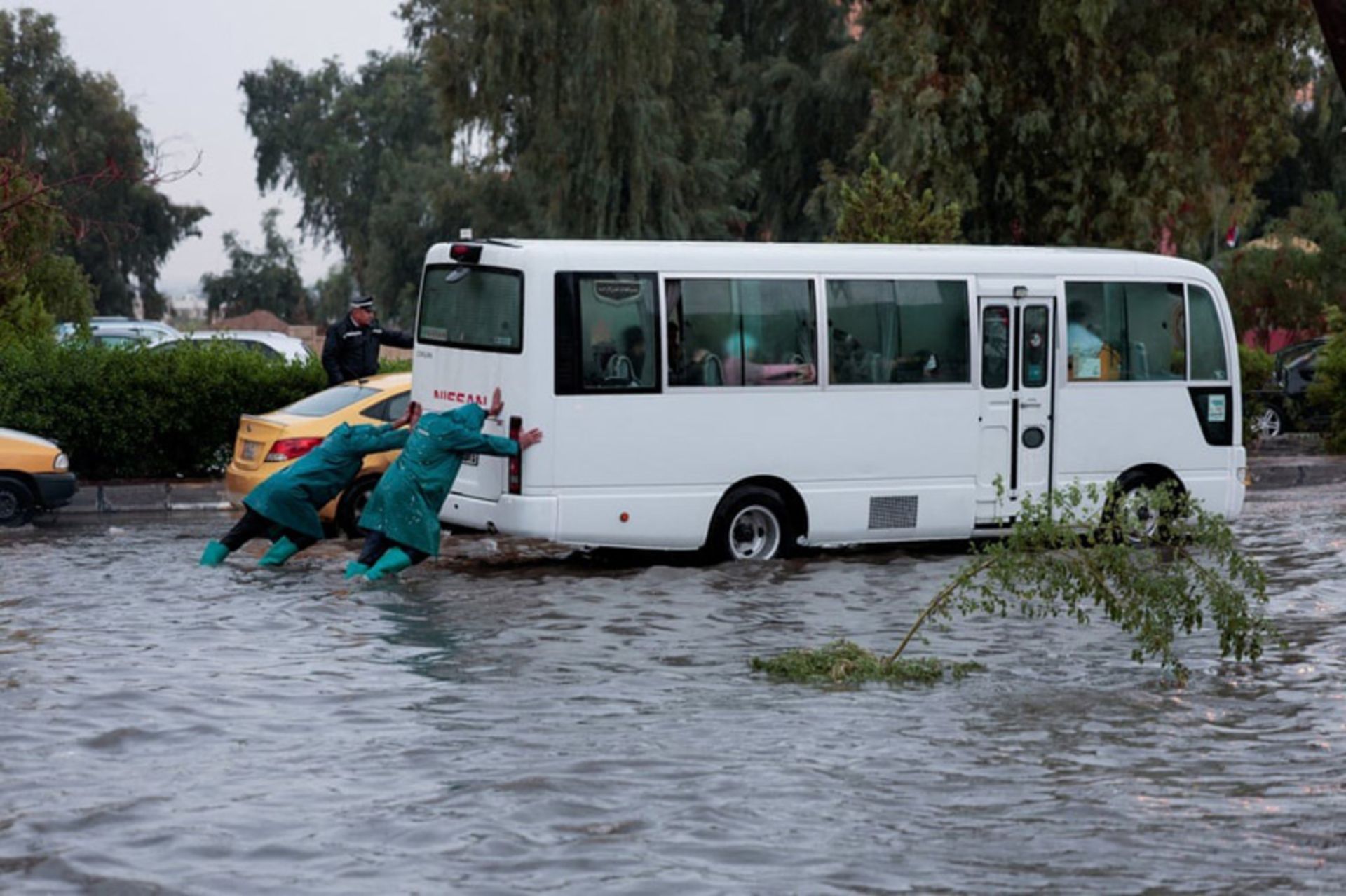 کارگران شهرداری پس از بارش شدید باران، اتوبوسی را از میان سیلاب عبور می‌دهند