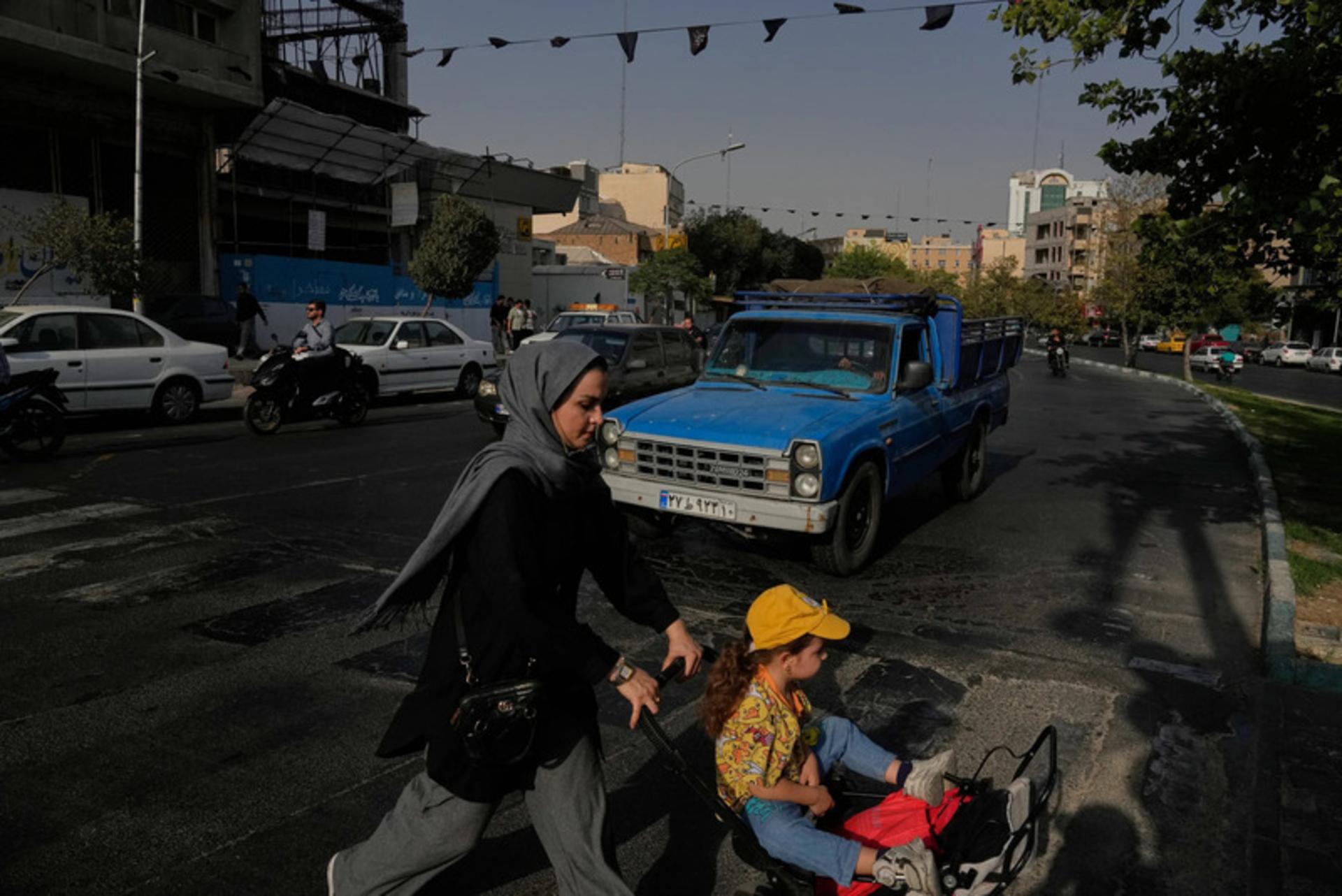 زنی با کودکش که در کالسکه است، از خیابان می‌گذرد