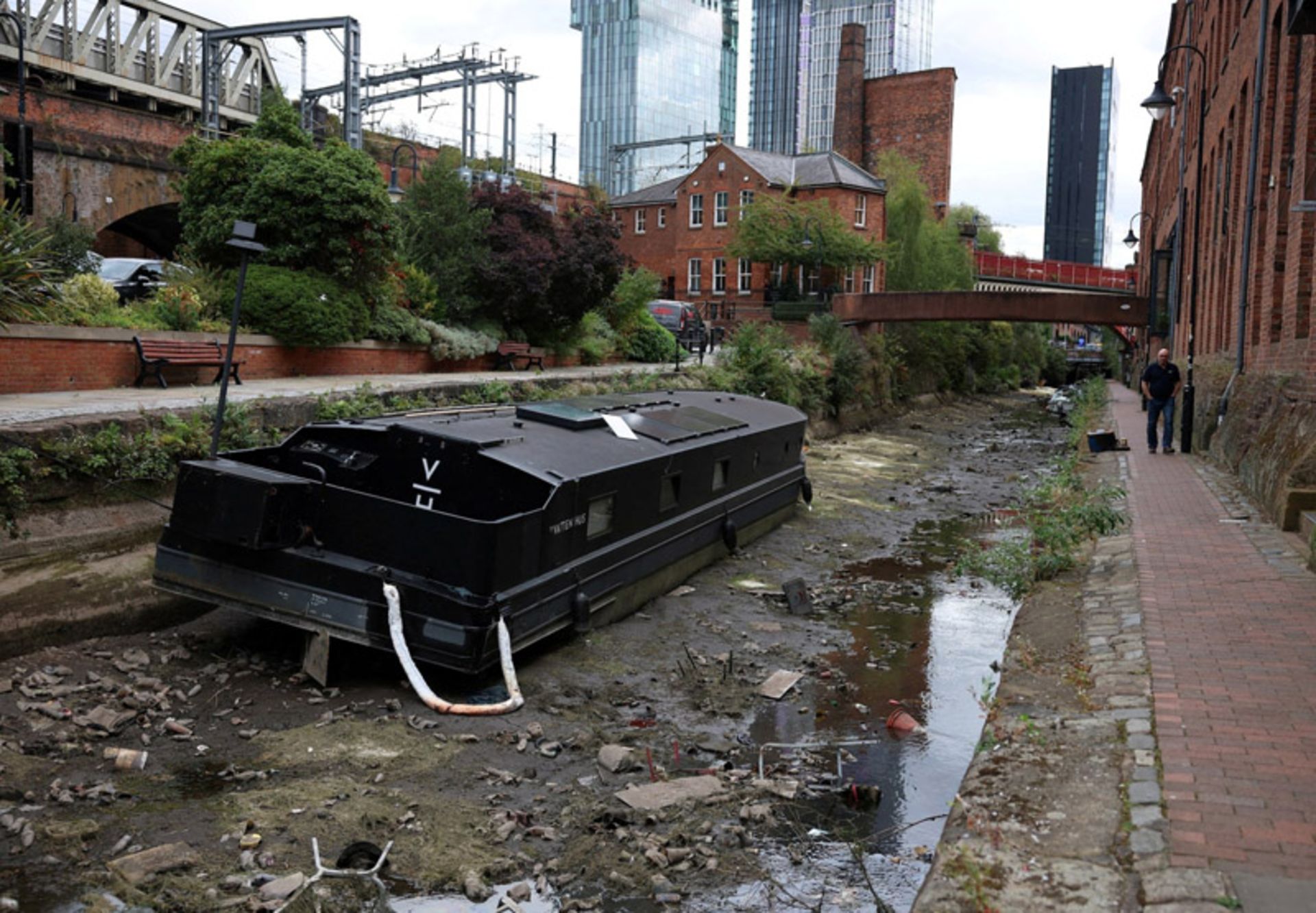 پیاده‌روی مردی از کنار قایق به گل نشسته در بخش خشک‌شده کانال روچدیل، منچستر