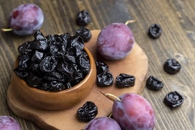برقوق خشک (Prunes) در ظرف چوبی در کنار میوه برقوق تازه