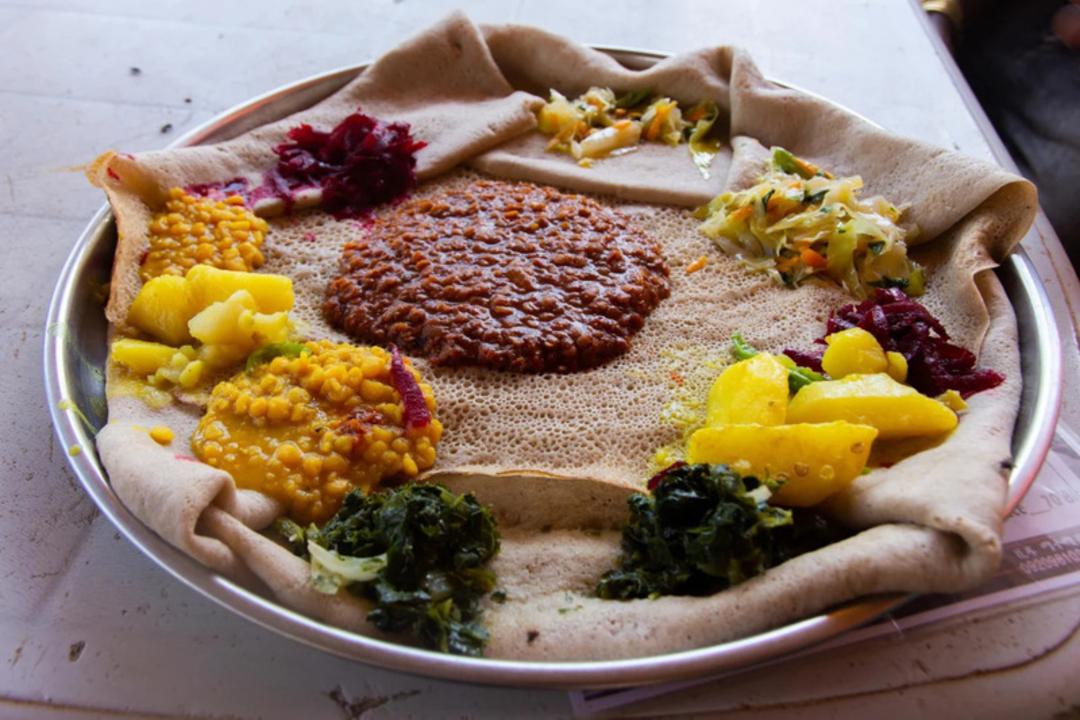 غذای سنتی اتیوپیایی شامل نان اینجرا (Injera) و انواع خوراک‌های گیاهی در یک بشقاب فلزی