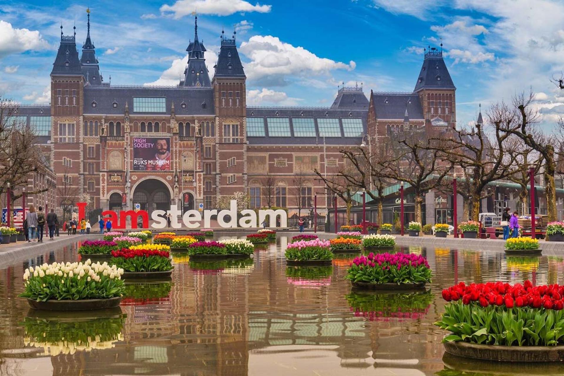 نمایی چشم‌نواز از میدان موزه در آمستردام با یک ساختمان تاریخی و لاله‌های رنگارنگ در پیش‌زمینه