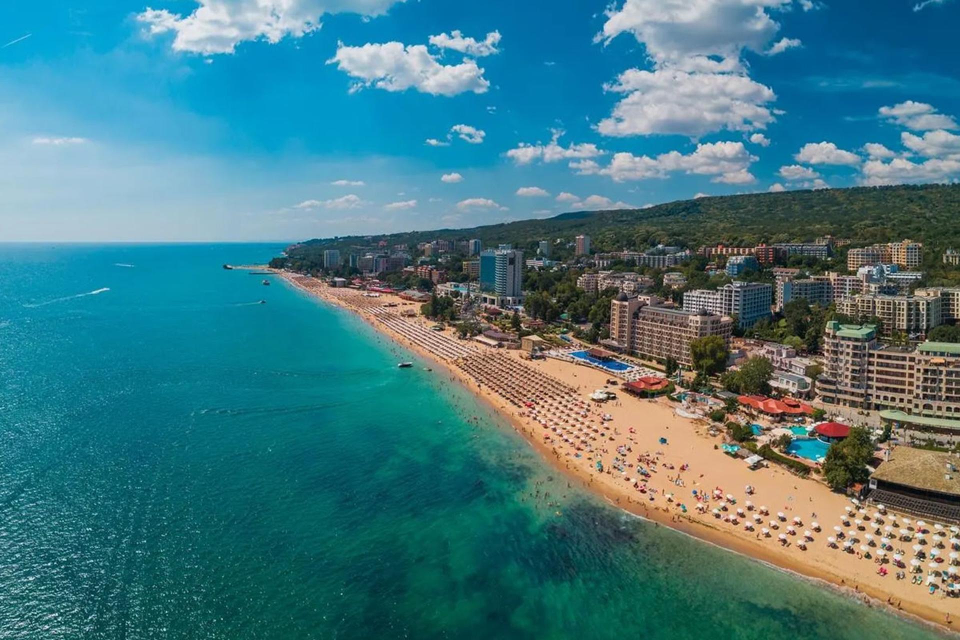 تصویر پانوراما از بالا از نوار ساحلی طولانی با ماسه‌های روشن و چترهای آفتابی ردیف شده