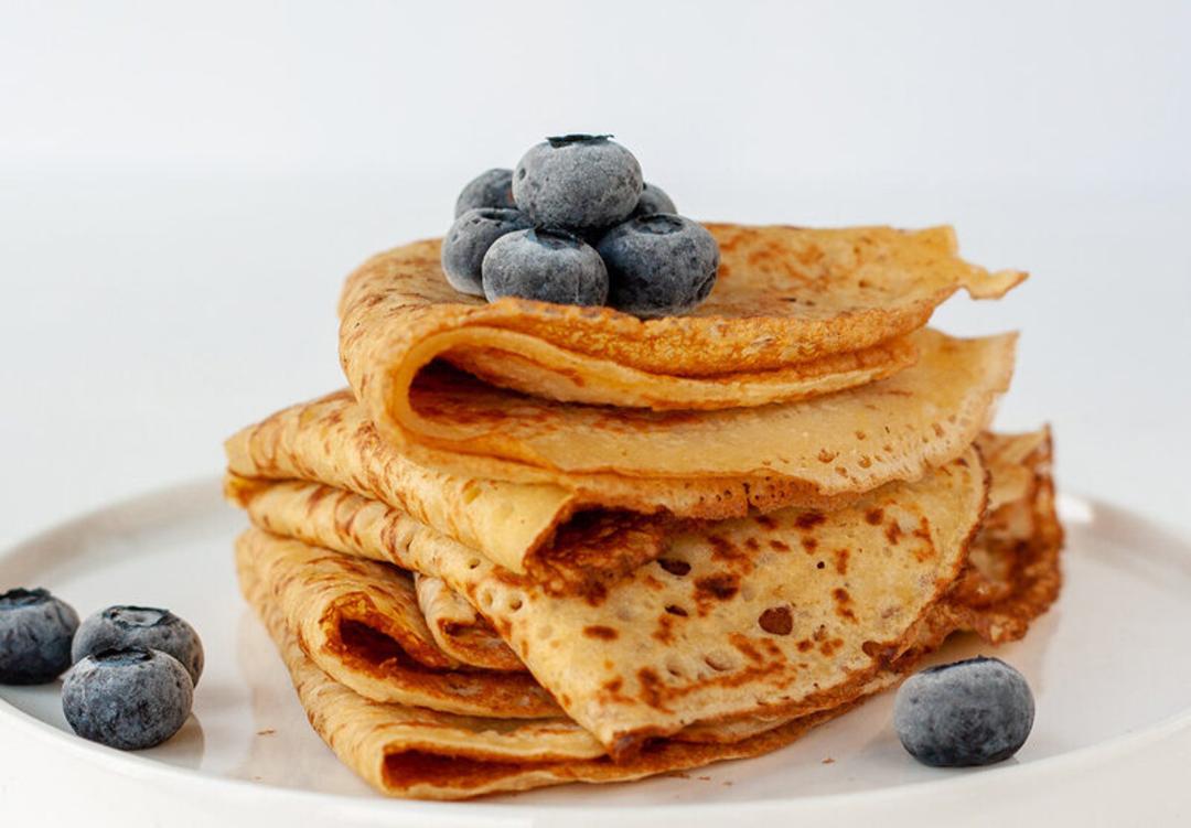 پنکیک فرانسوی (Crepe) روی بشقاب سفید همراه با دانه‌های بلوبری تازه