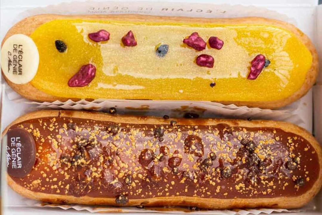 دو عدد شیرینی اکله (Éclair) با پوشش‌های زرد و قهوه‌ای روی جعبه