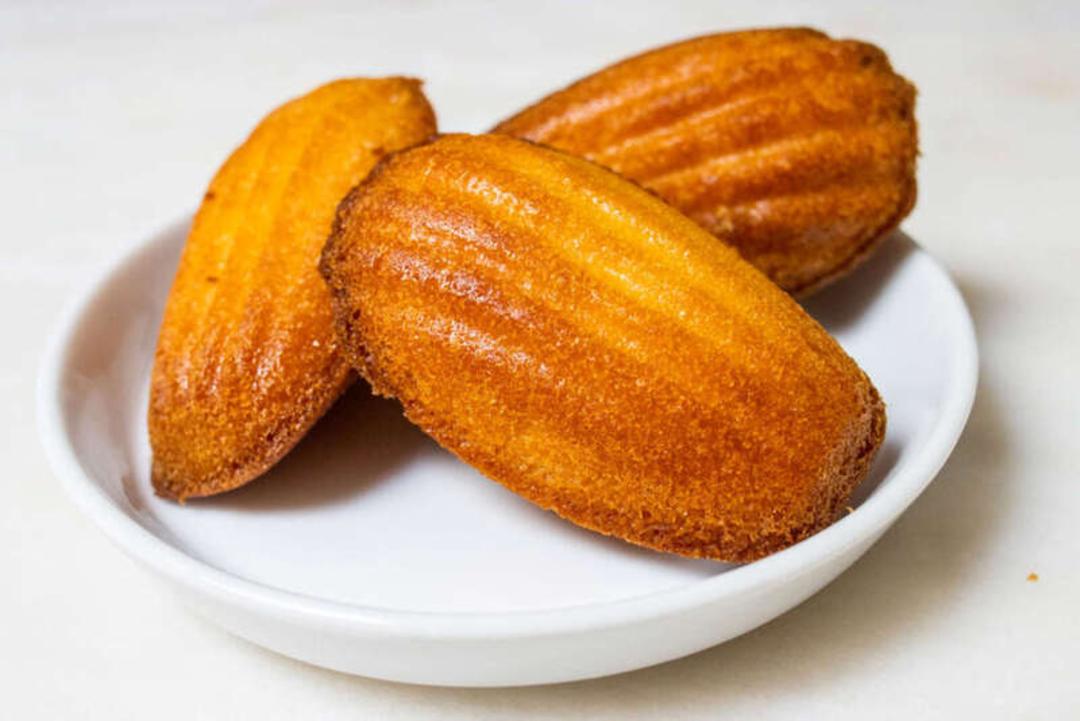 شیرینی مدیلن (Madeleine) طلایی رنگ در یک بشقاب سفید کوچک