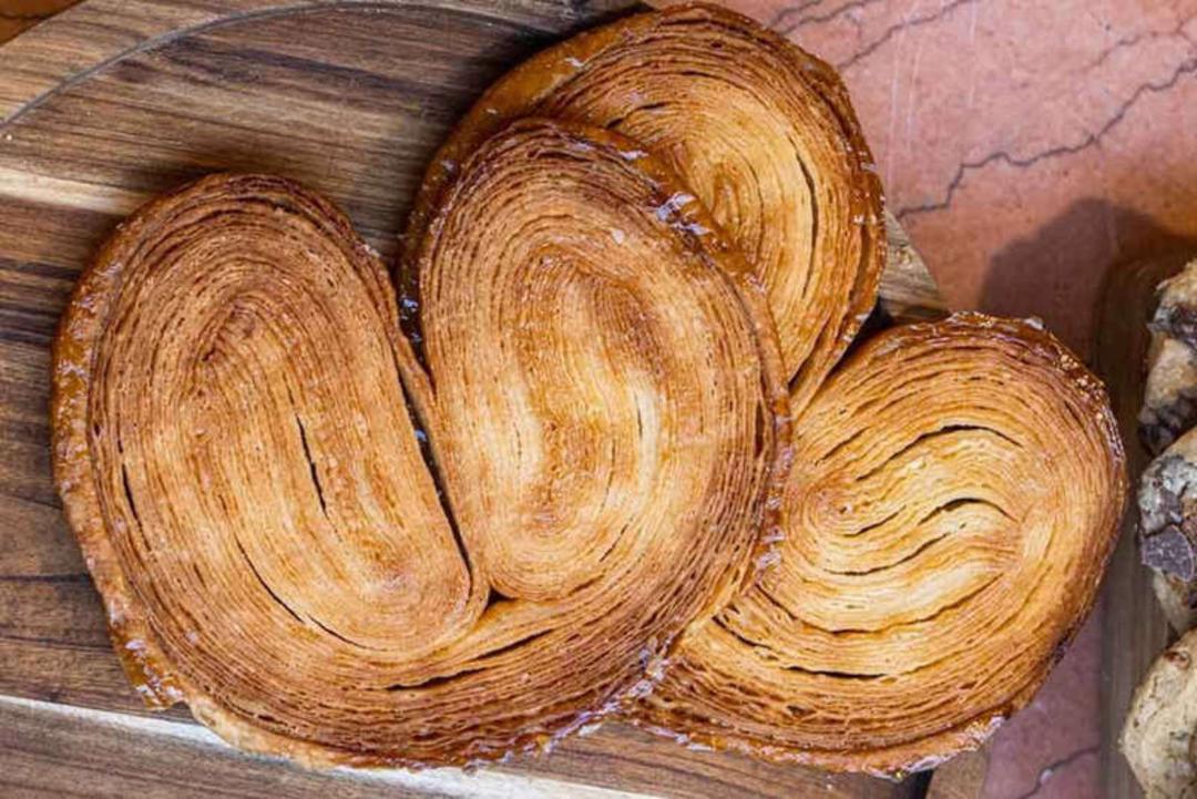 شیرینی پالمیر (Palmier) با لایه‌های ترد و کاراملی روی تخته چوبی