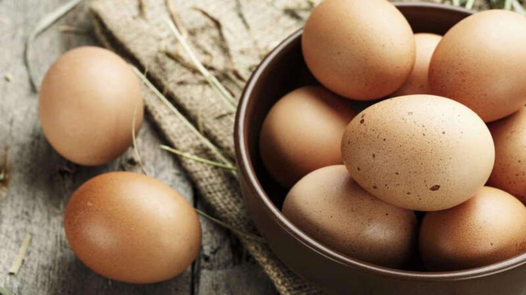 تخم‌مرغ‌های قهوه‌ای رنگ در یک ظرف و روی سطح چوبی