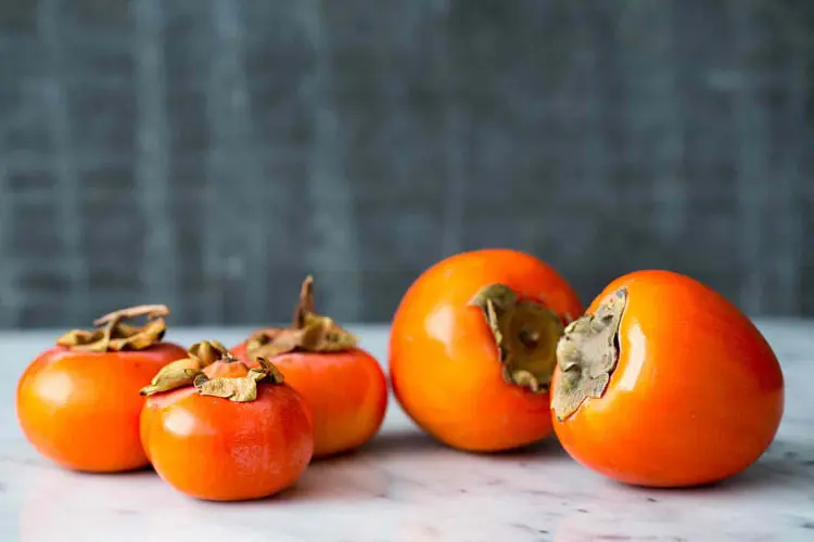 خرمالوی تازه و نارنجی رنگ روی سطح مرمر سفید