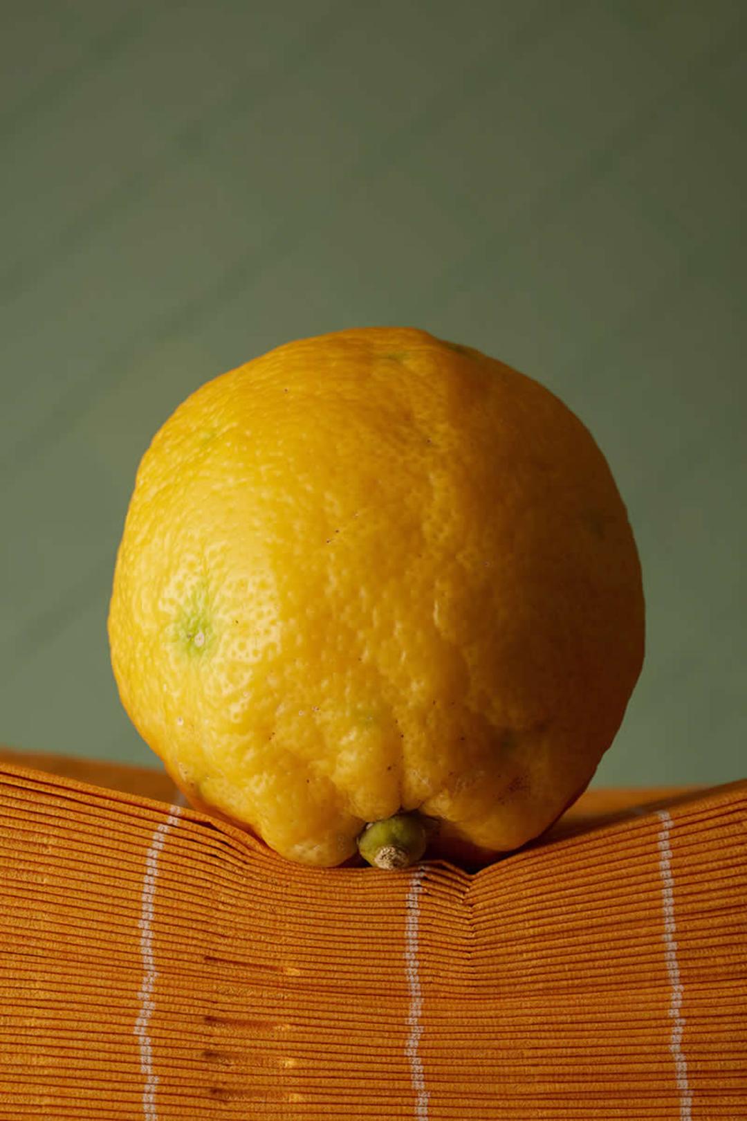 لیموی زرد (Lemon) با پوست بافت‌دار روی یک سطح نارنجی