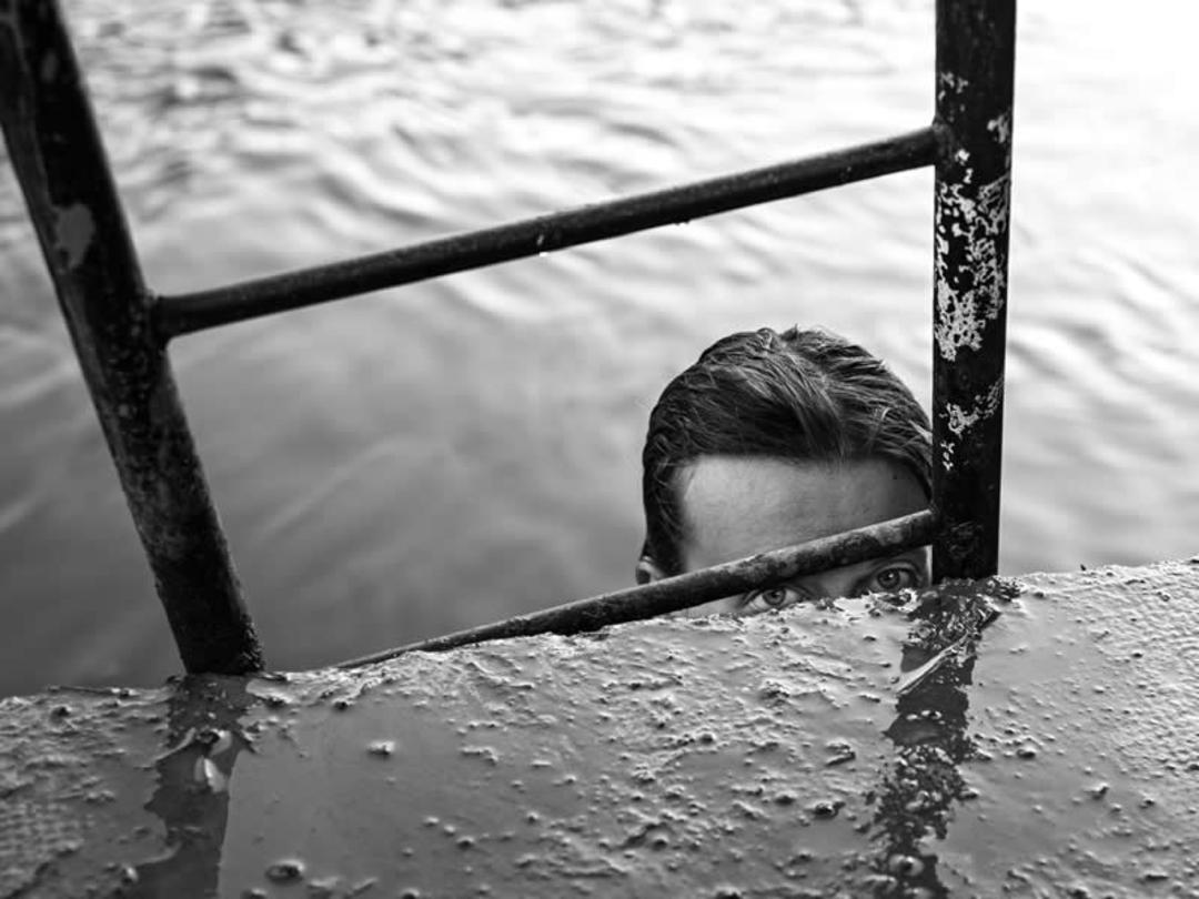 چهره مردی در میان نرده‌های فلزی و آب در پاریس