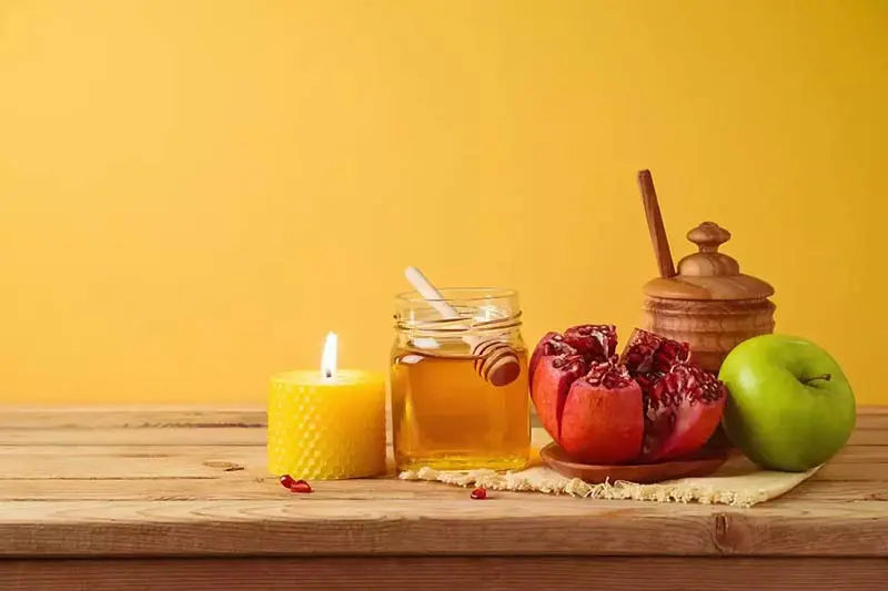 انار باز شده، سیب سبز، ظرف عسل و شمع روی میز چوبی