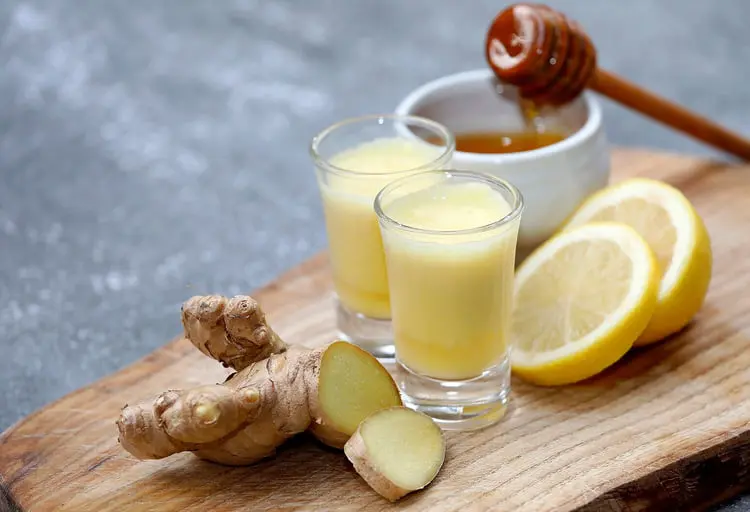 شات زنجبیل (Ginger) و لیمو در کنار تکه‌های زنجبیل تازه و عسل