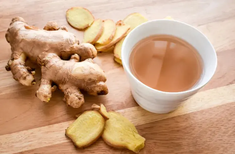 ریشه زنجبیل (Ginger) و فنجان چای زنجبیل روی میز چوبی