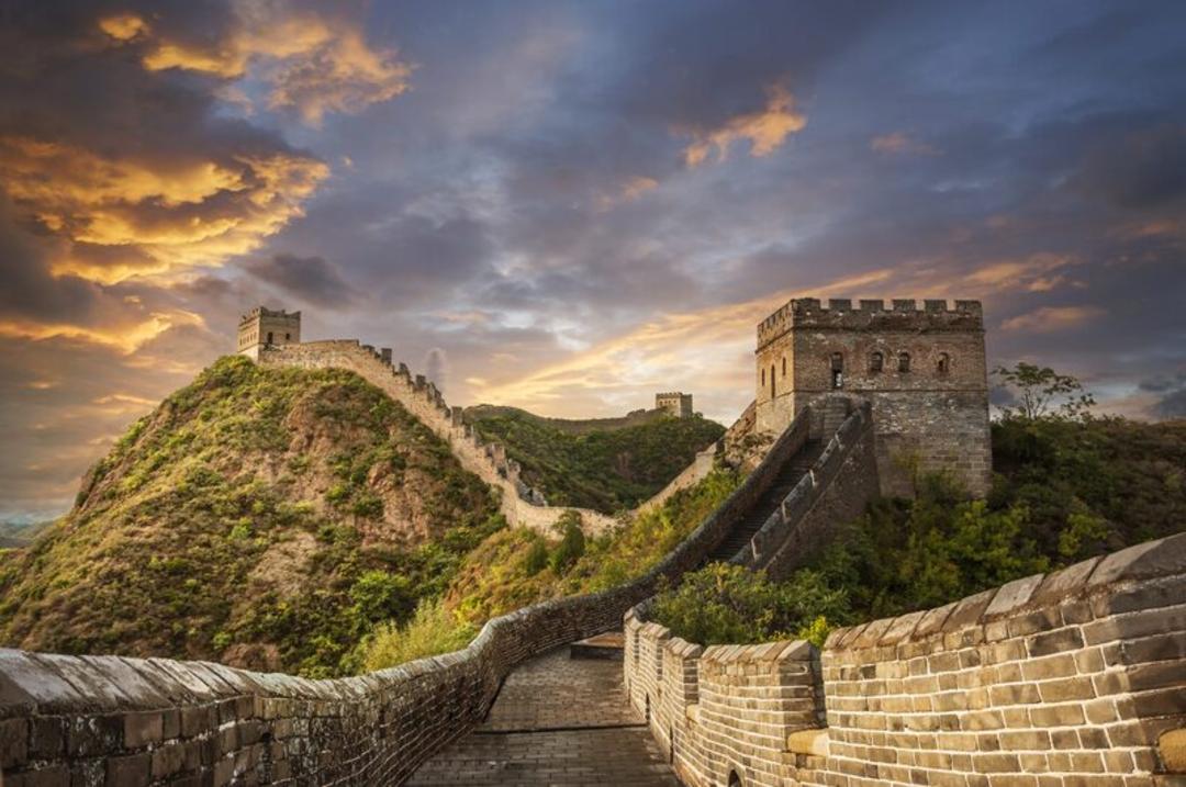 دیوار بزرگ چین (Great Wall of China) بر فراز تپه‌های سبز در زمان غروب خورشید
