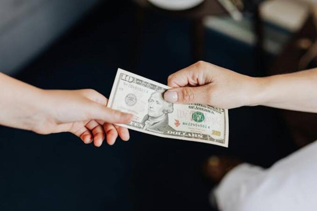 دست‌های دو نفر در حال رد و بدل کردن اسکناس یک دلاری آمریکا (United States Dollar)