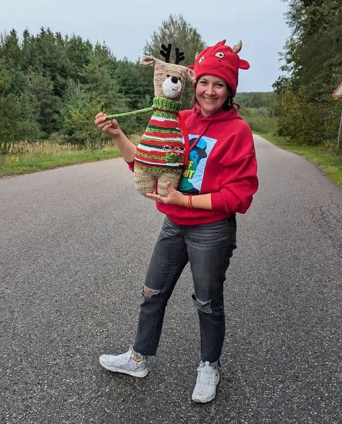 عروسک گوزن بافتنی (Crochet Deer) با لباس رنگارنگ در دست یک زن