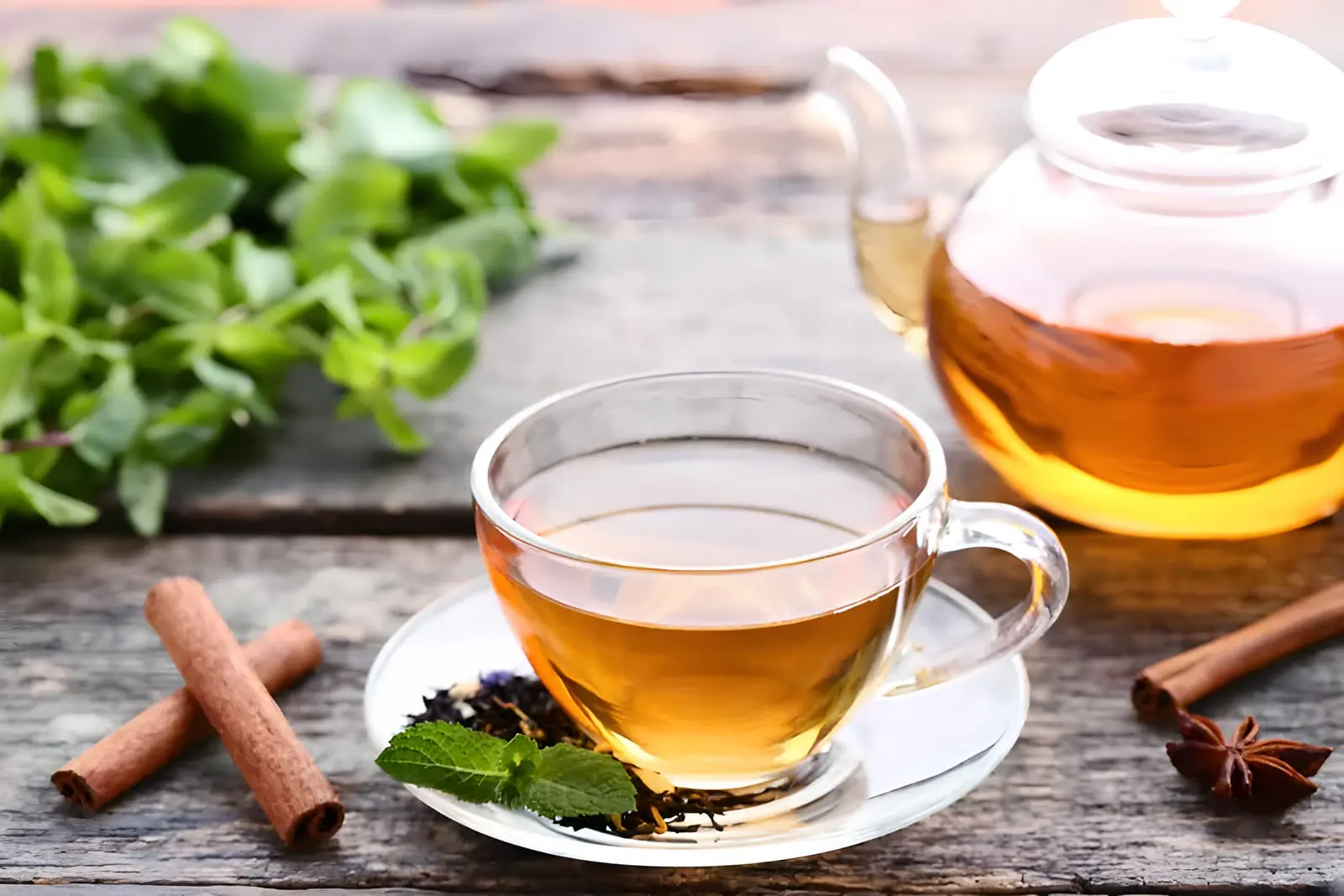 فنجان چای گیاهی در کنار دارچین و برگ‌های نعنا روی میز چوبی