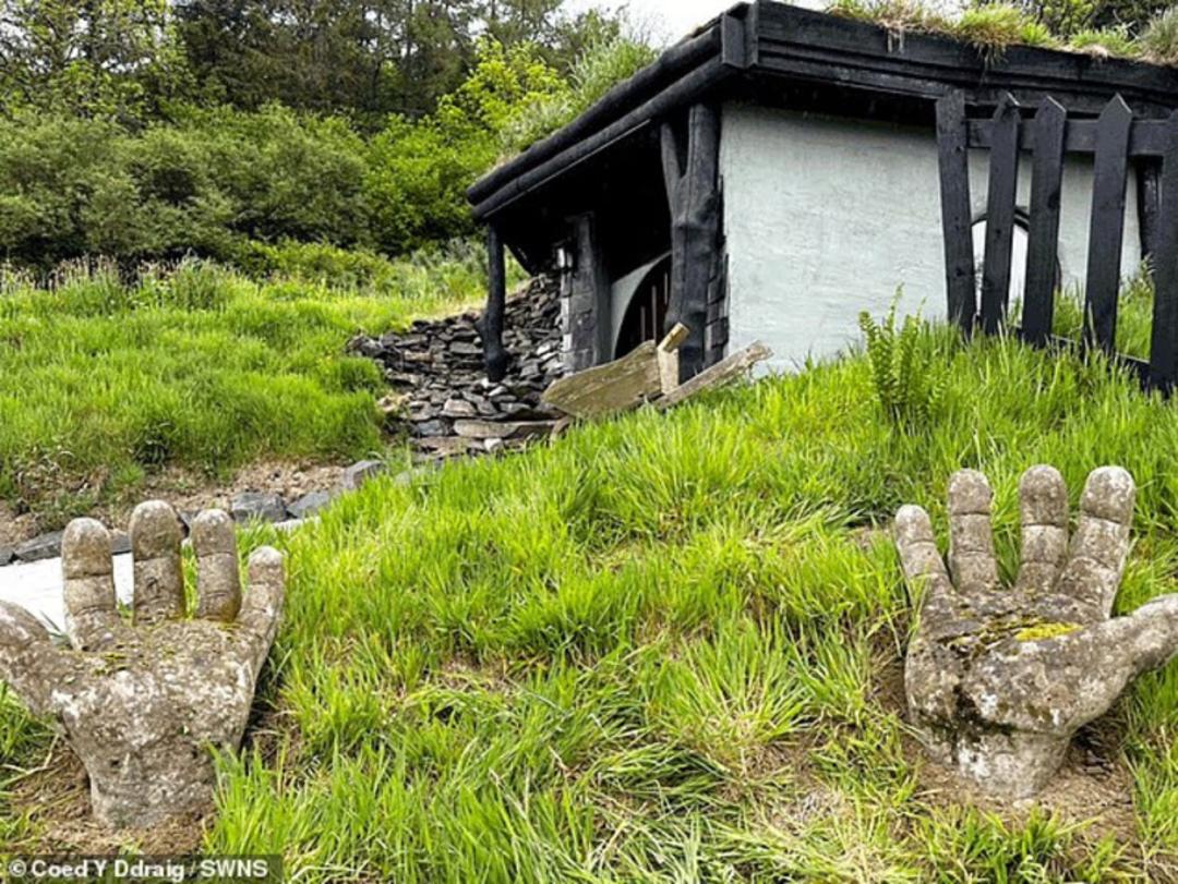 دهکده هابیتی (Hobbiton) با نمای تپه‌ای و مجسمه‌های سنگی دست در چمنزار