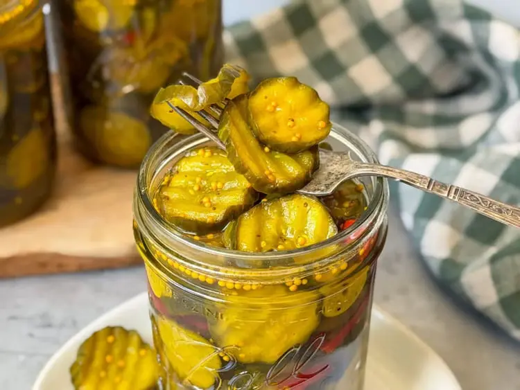 خیارشور خانگی ترد در ظرف شیشه‌ای که با چنگال برداشته شده است