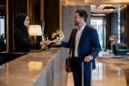 یک مرد مسافر در حال تحویل کارت به کارمند زن با حجاب در میز پذیرش هتل