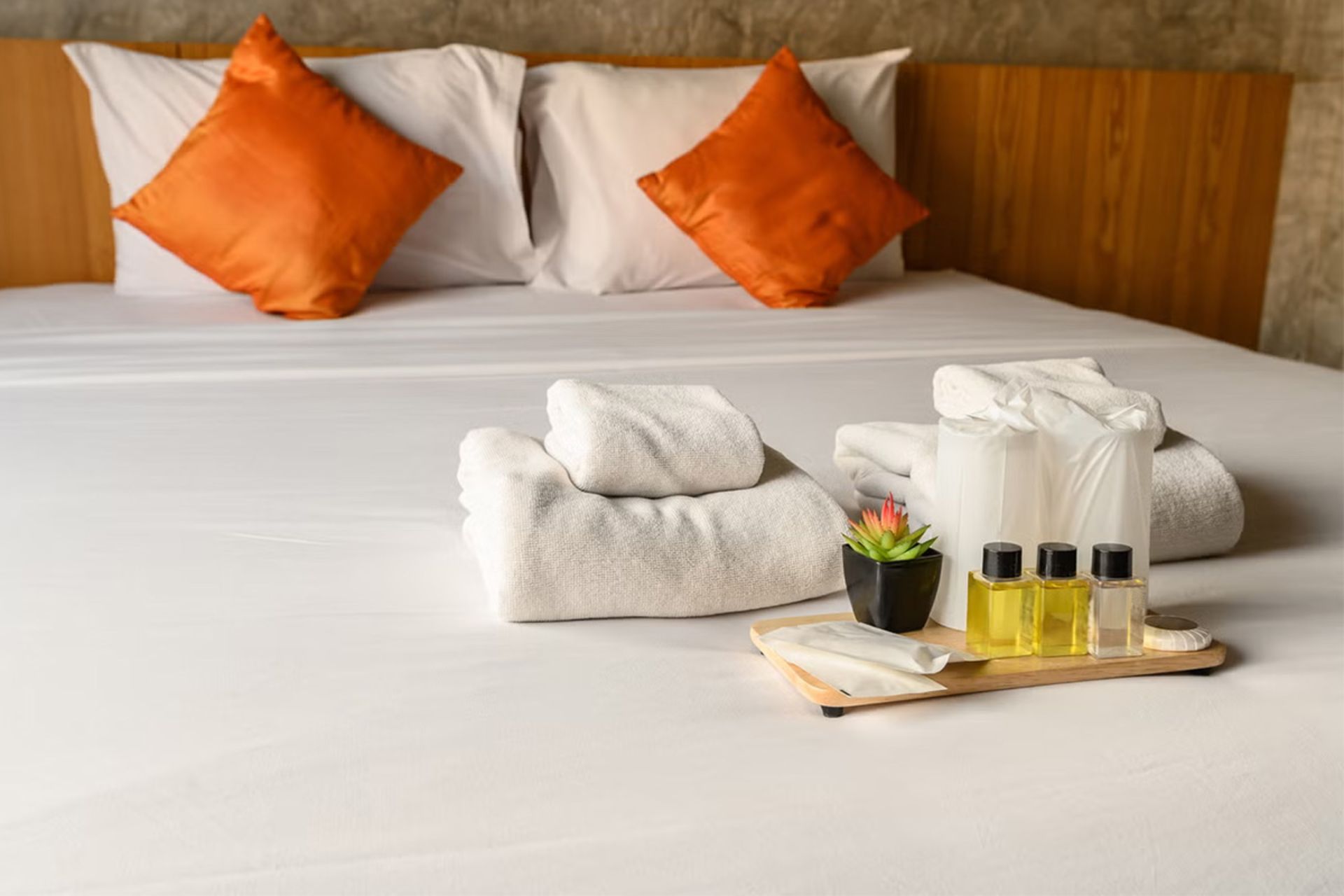 سینی لوازم بهداشتی و حوله‌های تاشده روی تخت مرتب‌شده هتل