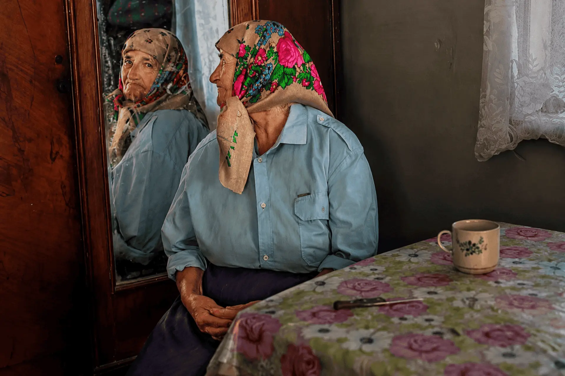 پیرزن اوکراینی با روسری رنگی به آینه خانه‌ش نگاه می‌کند