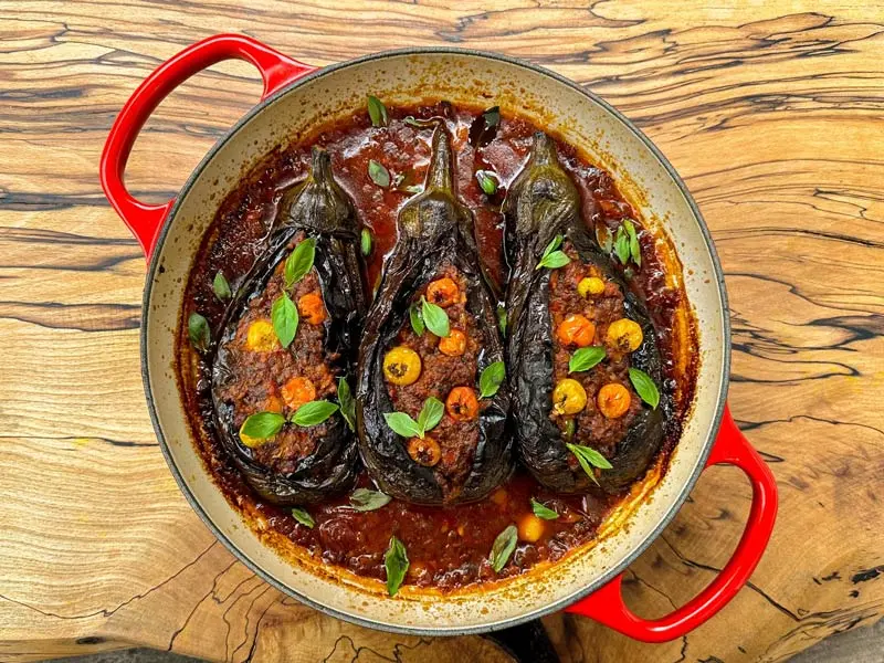 سه عدد بادمجان شکم‌پر بزرگ در یک تابه با سس غلیظ گوجه‌فرنگی