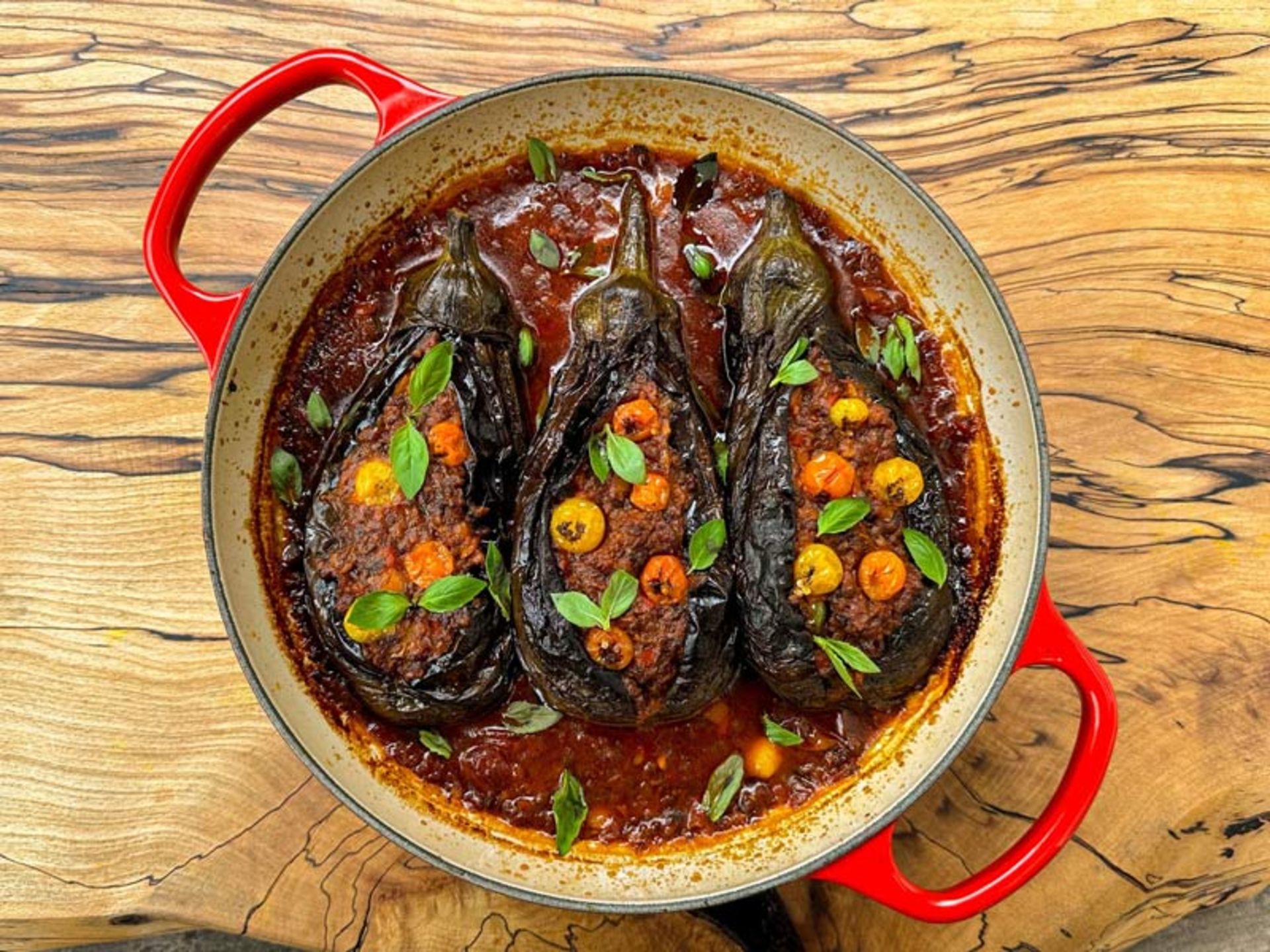 سه عدد بادمجان شکم‌پر بزرگ در یک تابه با سس غلیظ گوجه‌فرنگی