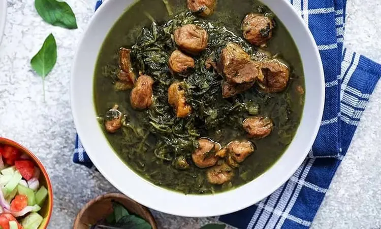 خورش آلو اسفناج شامل اسفناج پخته و تکه‌های گوشت در ظرف سفید