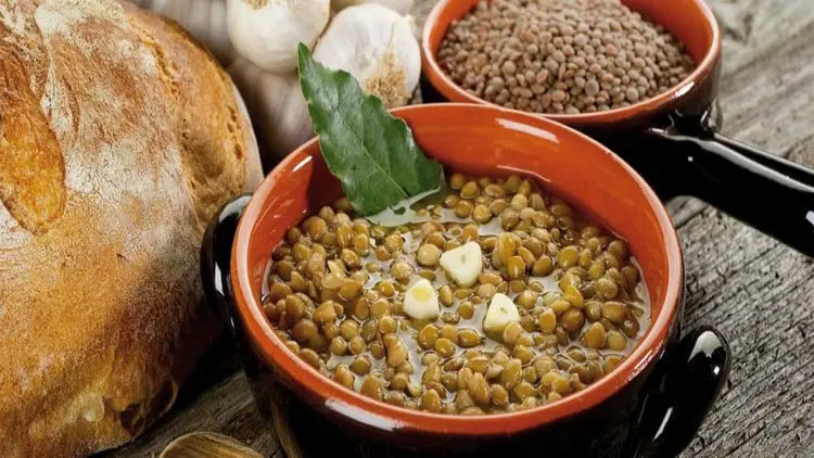 خورش عدسی پخته شده در ظرف سفالی همراه با نان و سیر