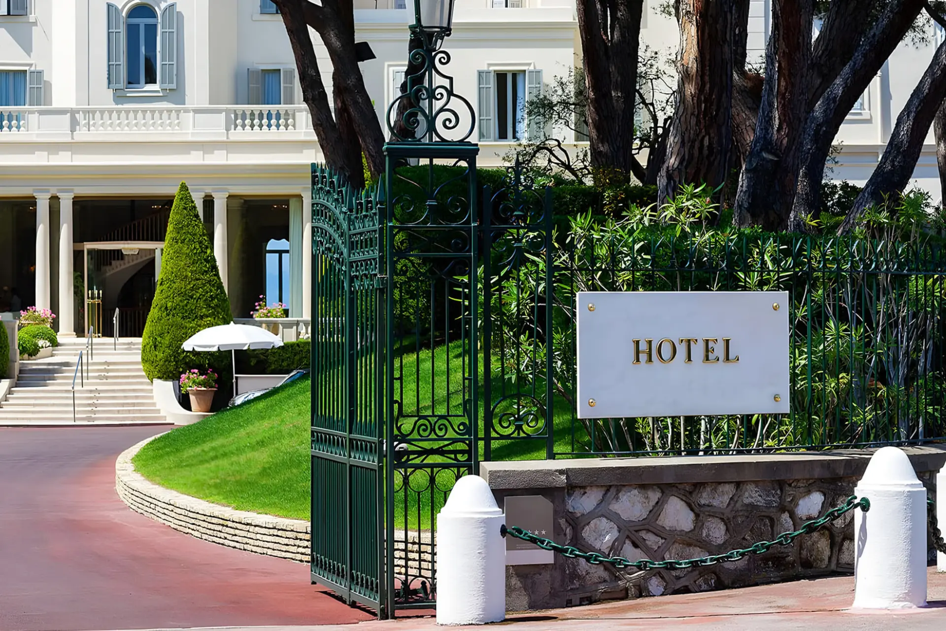 ورودی اصلی یک هتل لوکس (Hotel) با نرده‌های آهنی سبز و تابلوی سفید