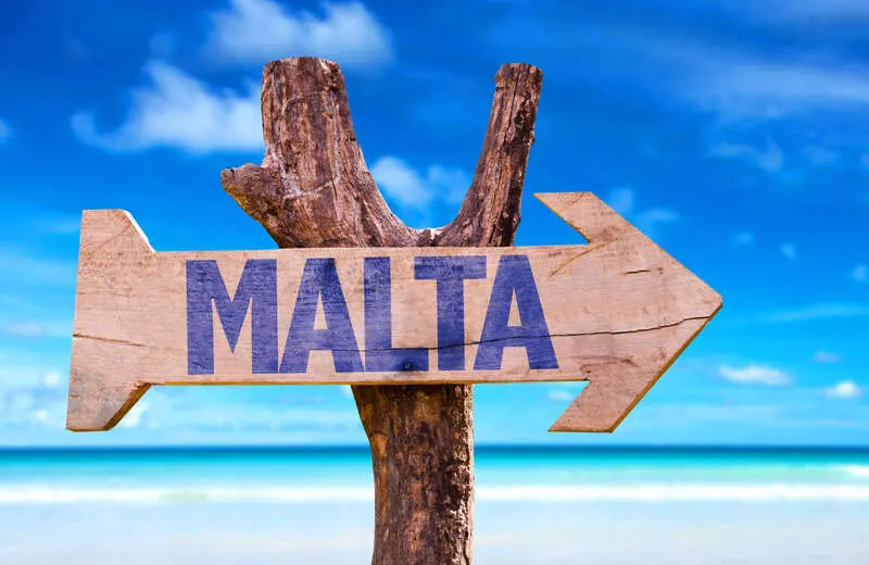 تابلوی چوبی با نوشته مالتا (Malta) در مقابل ساحل و آسمان آبی